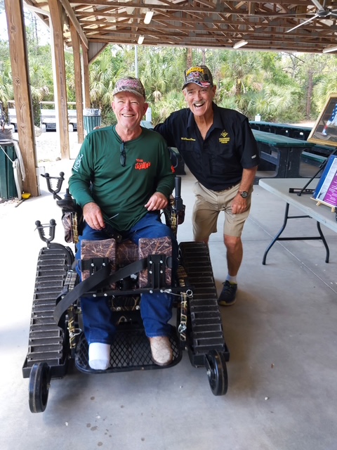 Veteran in all-terrain track chair with event coordinator